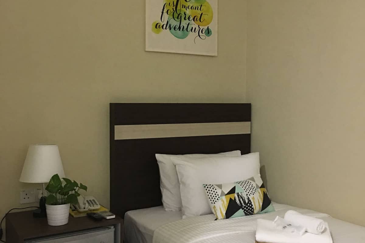 Une chambre d’hôtel avec un lit, une table de chevet avec une lampe et un téléphone, une petite armoire et une citation inspirante sur le mur.