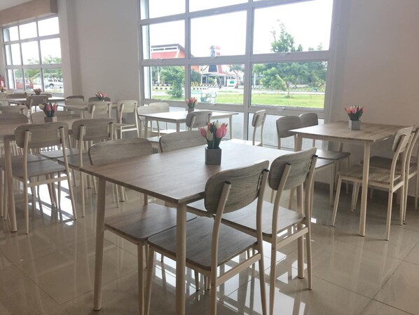 A spacious dining area with multiple tables and chairs, large windows offering a view of the outdoors, and a clean, modern design.