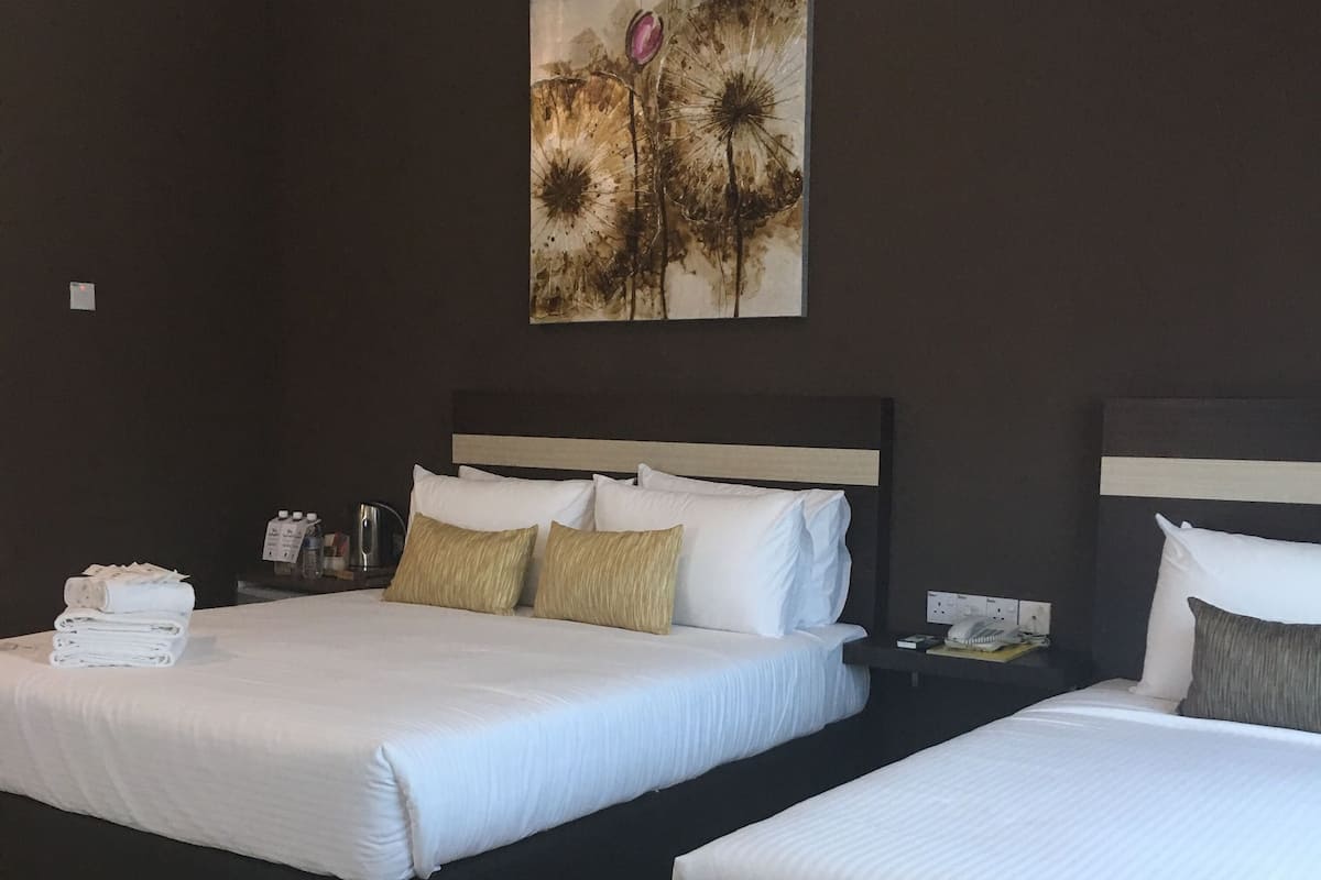 Une chambre d’hôtel avec deux lits, une table de chevet avec un téléphone et une lampe, et un tableau accroché au mur.