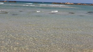 Una playa con aguas transparentes y poco profundas, y formaciones rocosas a lo lejos.