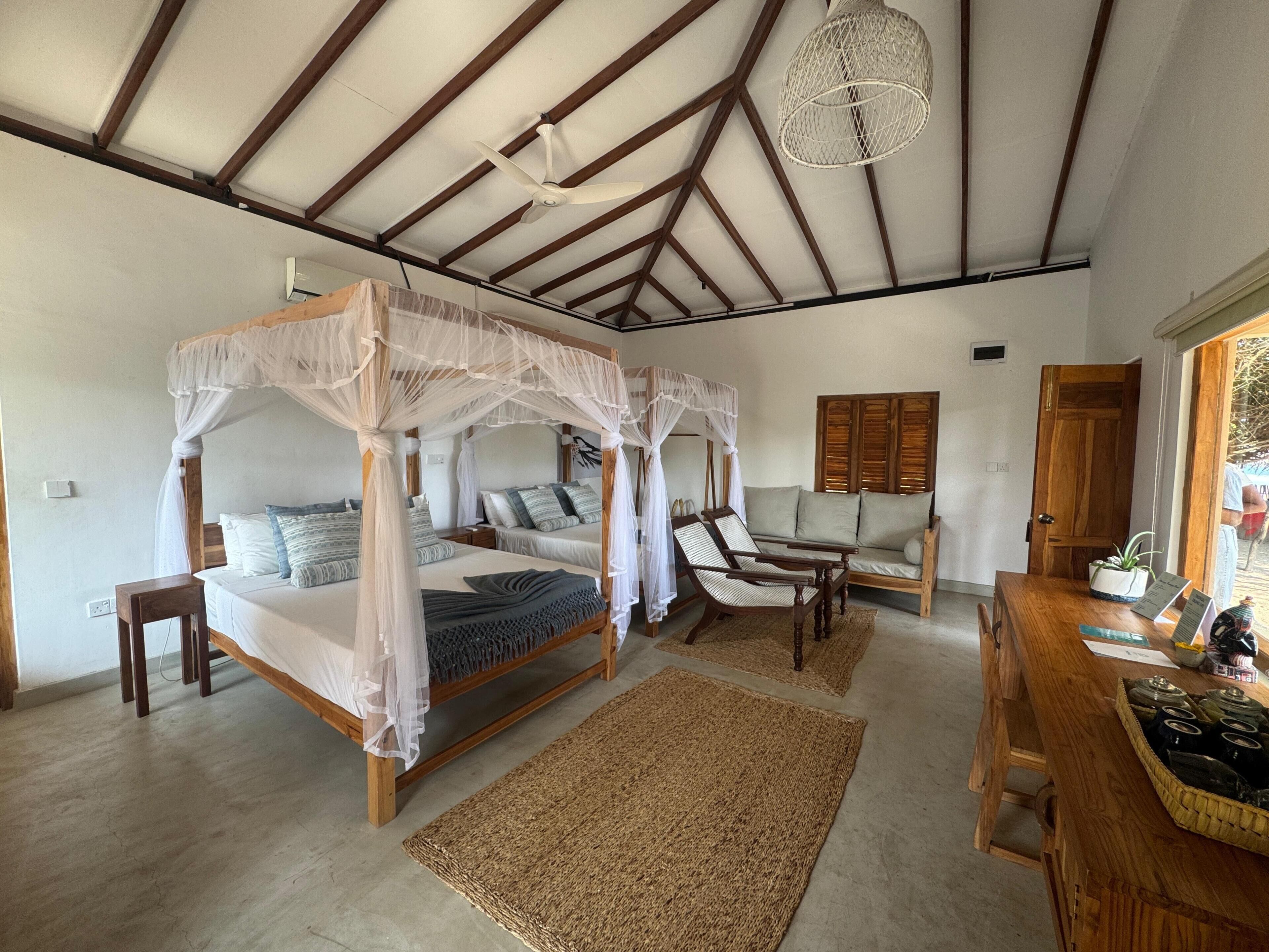 A room with a four-poster bed, a wooden sofa, a dining table, and a ceiling fan.