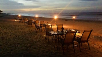 Mobiliario de comedor al aire libre con mesas y sillas dispuesto frente a la playa.