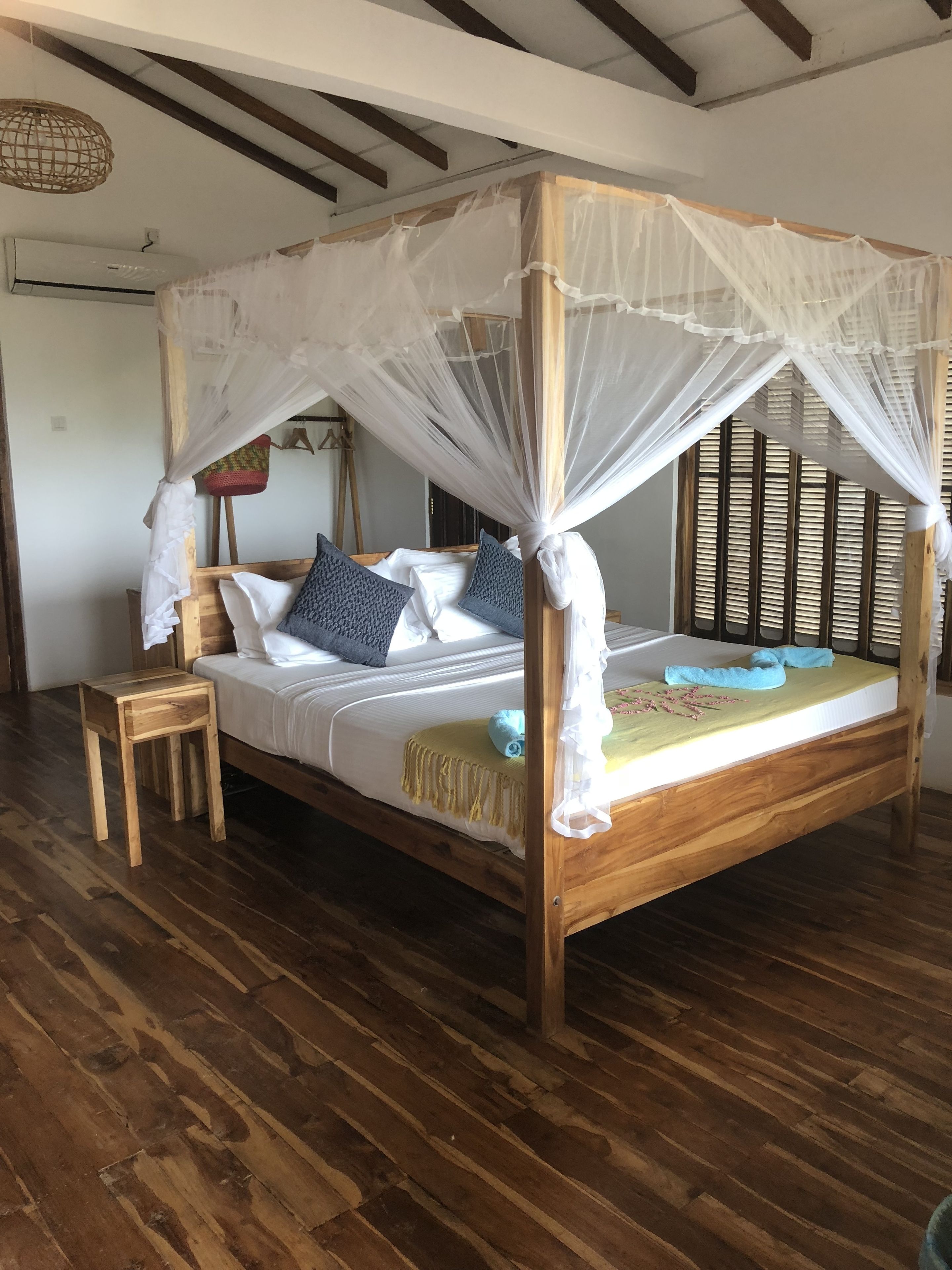 Ein hölzernes Himmelbett mit Baldachin, ein Nachttisch und ein kleiner Hocker.