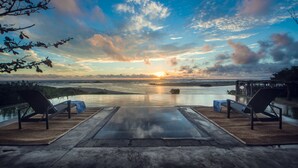 Una piscina infinita con dos sillas de descanso frente a un atardecer sobre el océano.