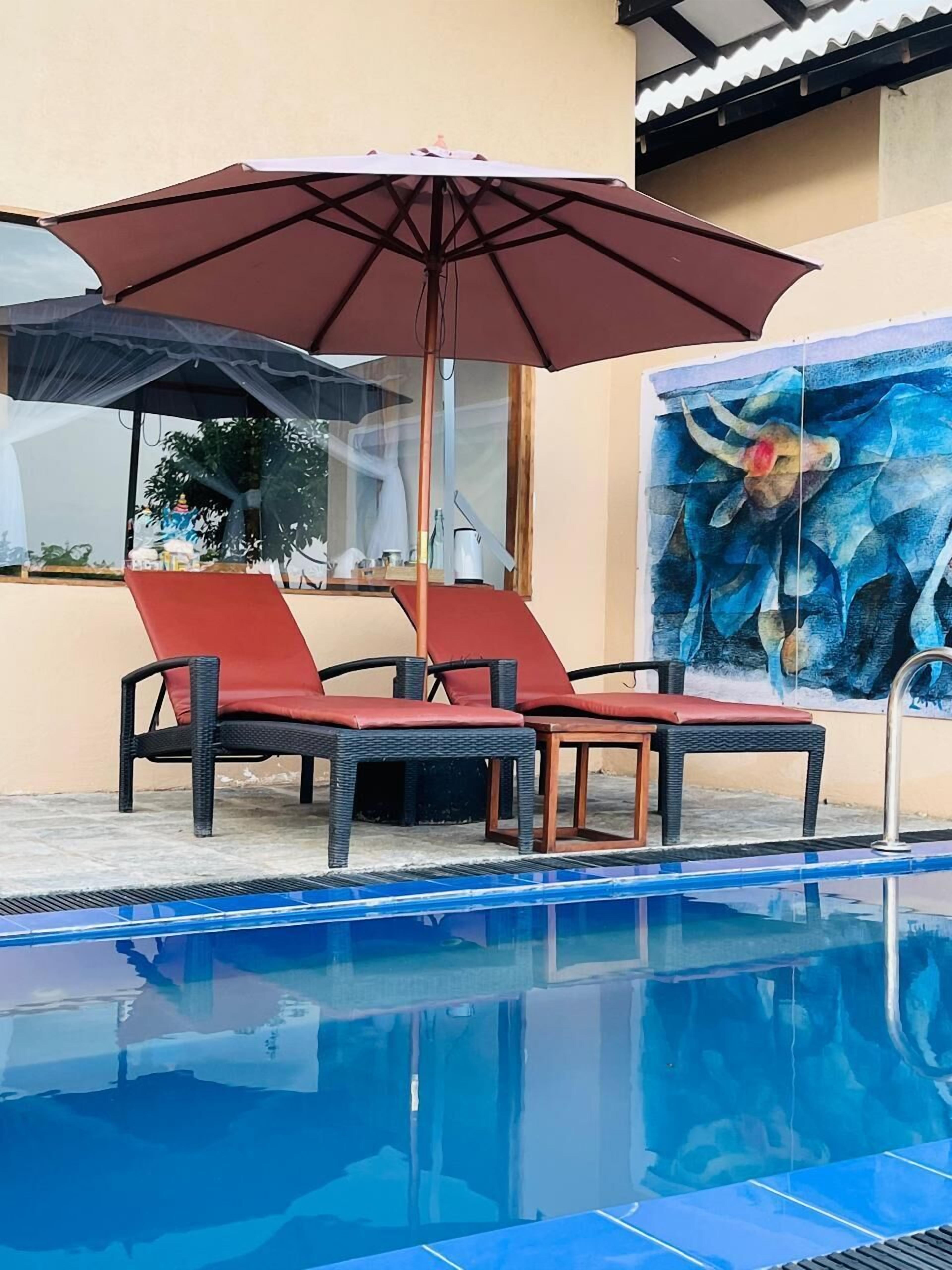 A pool area with lounge chairs and a large umbrella.