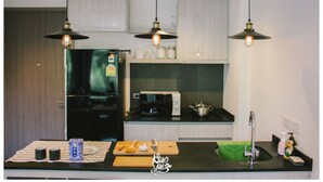 A modern kitchen with a black refrigerator, a microwave, and a stove. There are hanging lights, a cutting board with a knife, and a sink with a green towel.