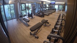 A modern gym with cardio machines, weight benches, and a TV screen.