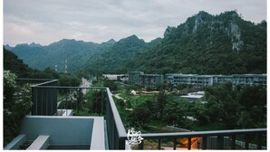 A view of a modern building complex with multiple floors, surrounded by lush greenery and mountains in the background.