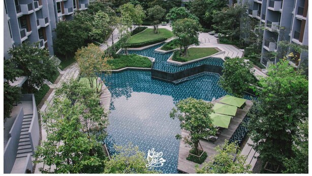 A modern residential complex with a central courtyard featuring a swimming pool, surrounded by lush greenery and multi-story buildings.