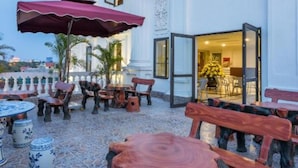 An outdoor seating area with wooden tables and chairs, a red umbrella, and a building with a white facade and columns. - Tan An Palace (Hai Phong)
