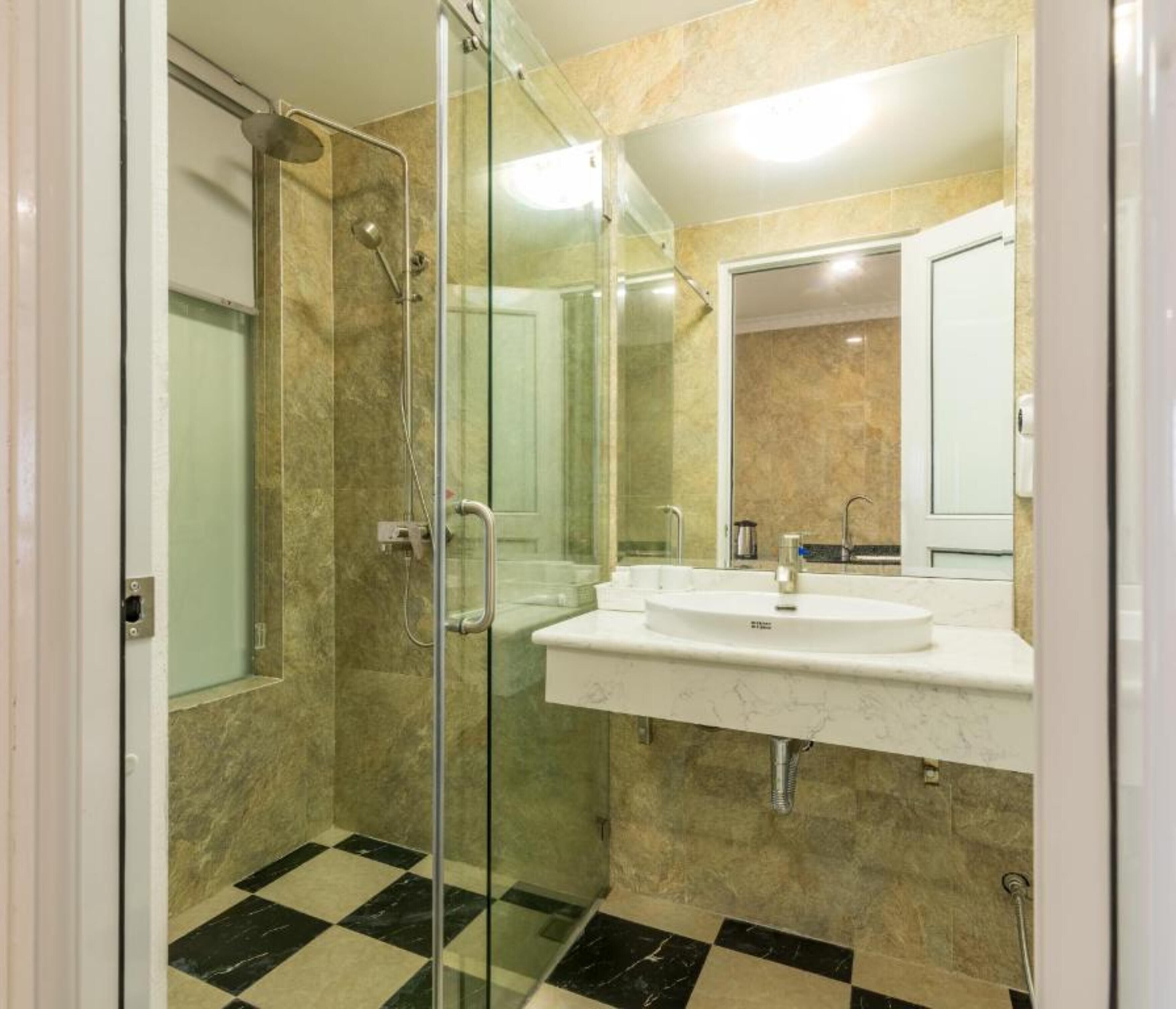Un baño moderno con cabina de ducha de vidrio, un lavamanos blanco con espejo y un piso con estampado de cuadros.
