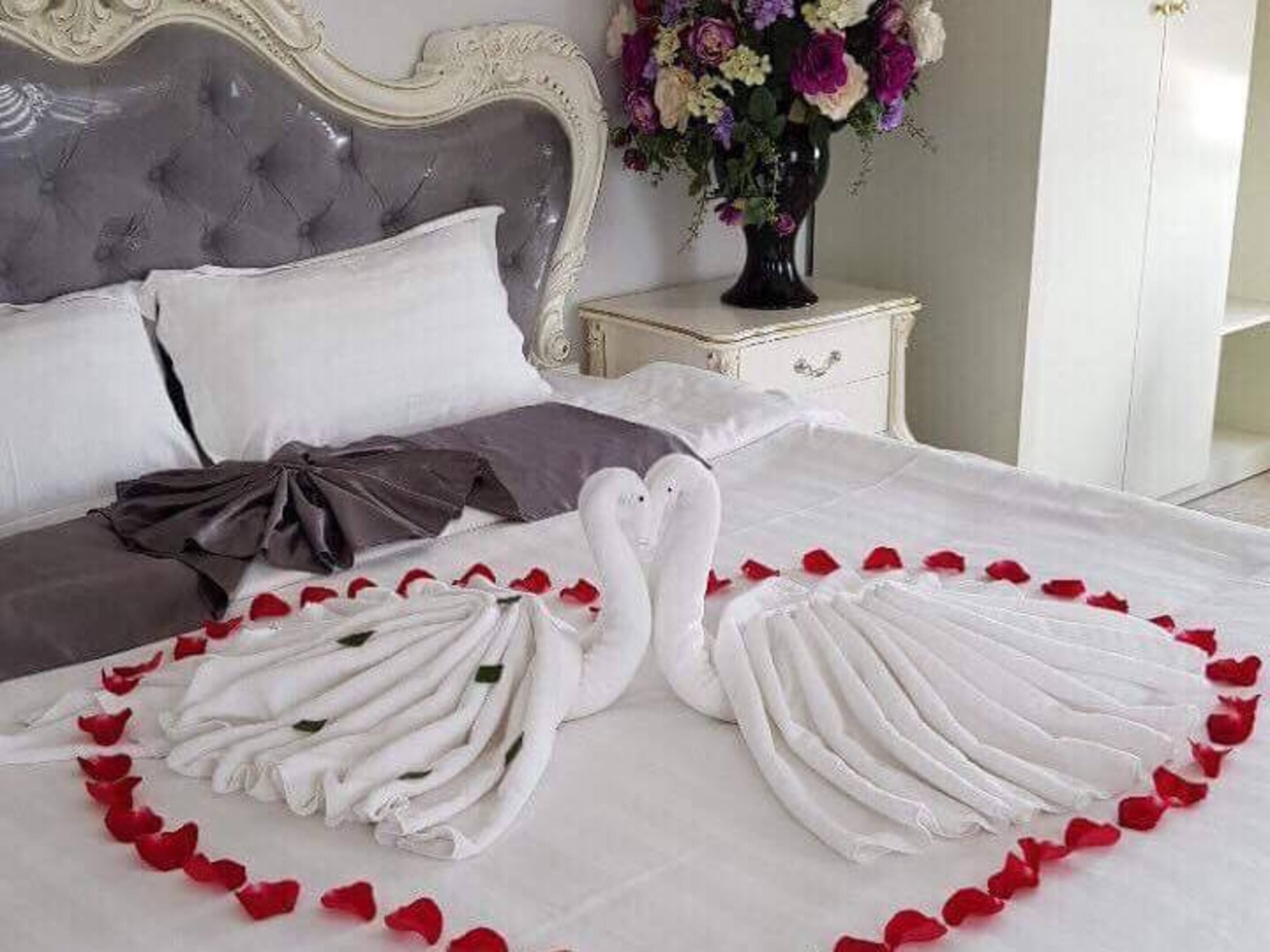 Una cama bien tendida con toallas dispuestas en forma de cisnes y corazones, un jarrón de flores y un cabecero clásico capitonado.