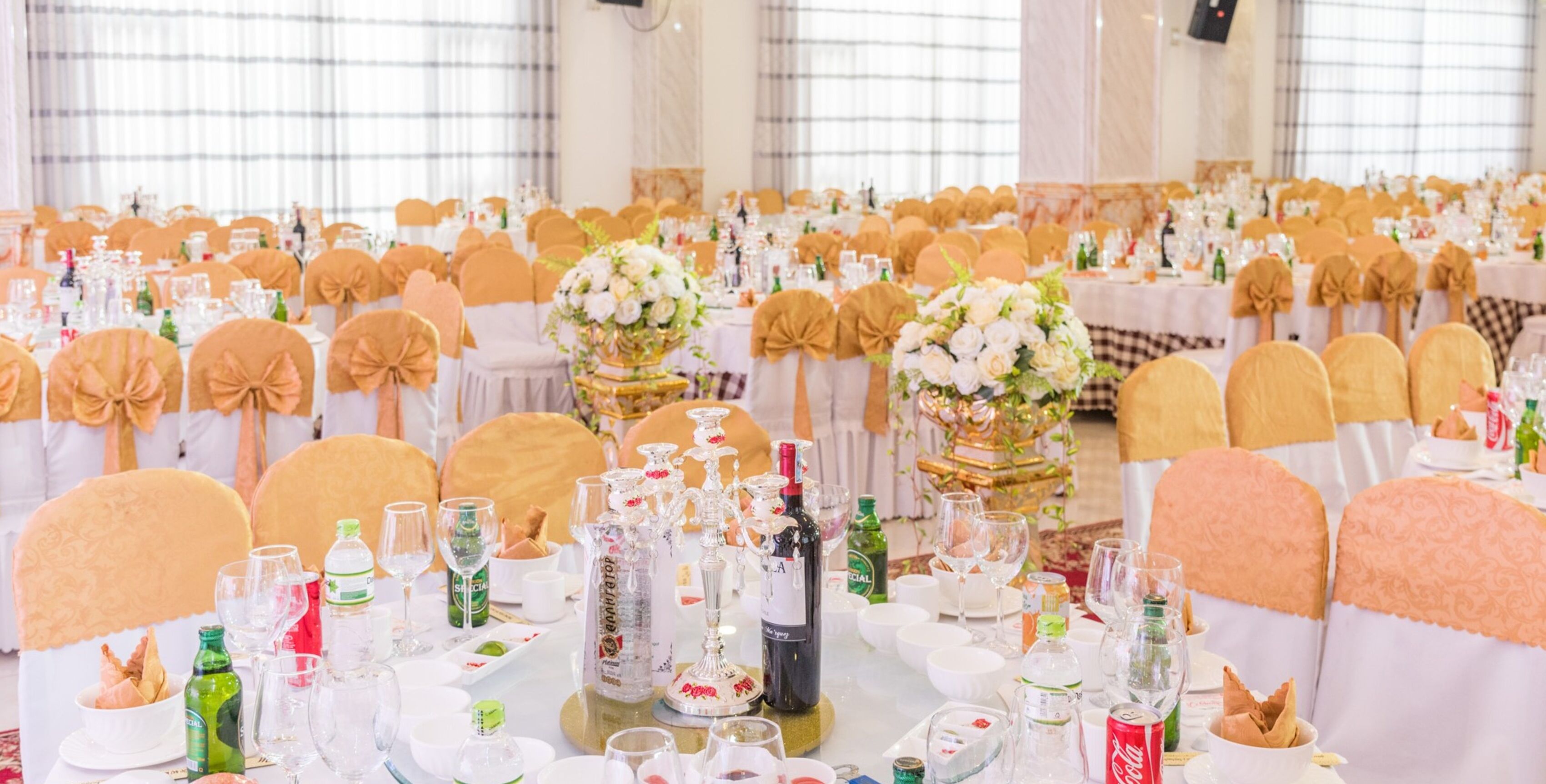 A banquet hall with round tables set for a formal event, adorned with floral centerpieces and various tableware.