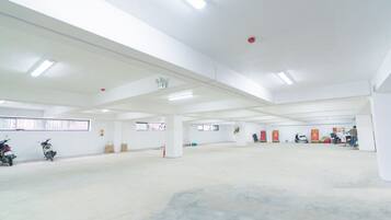 A spacious indoor area with white walls and ceiling, fluorescent lighting, and several motorcycles parked against the walls.