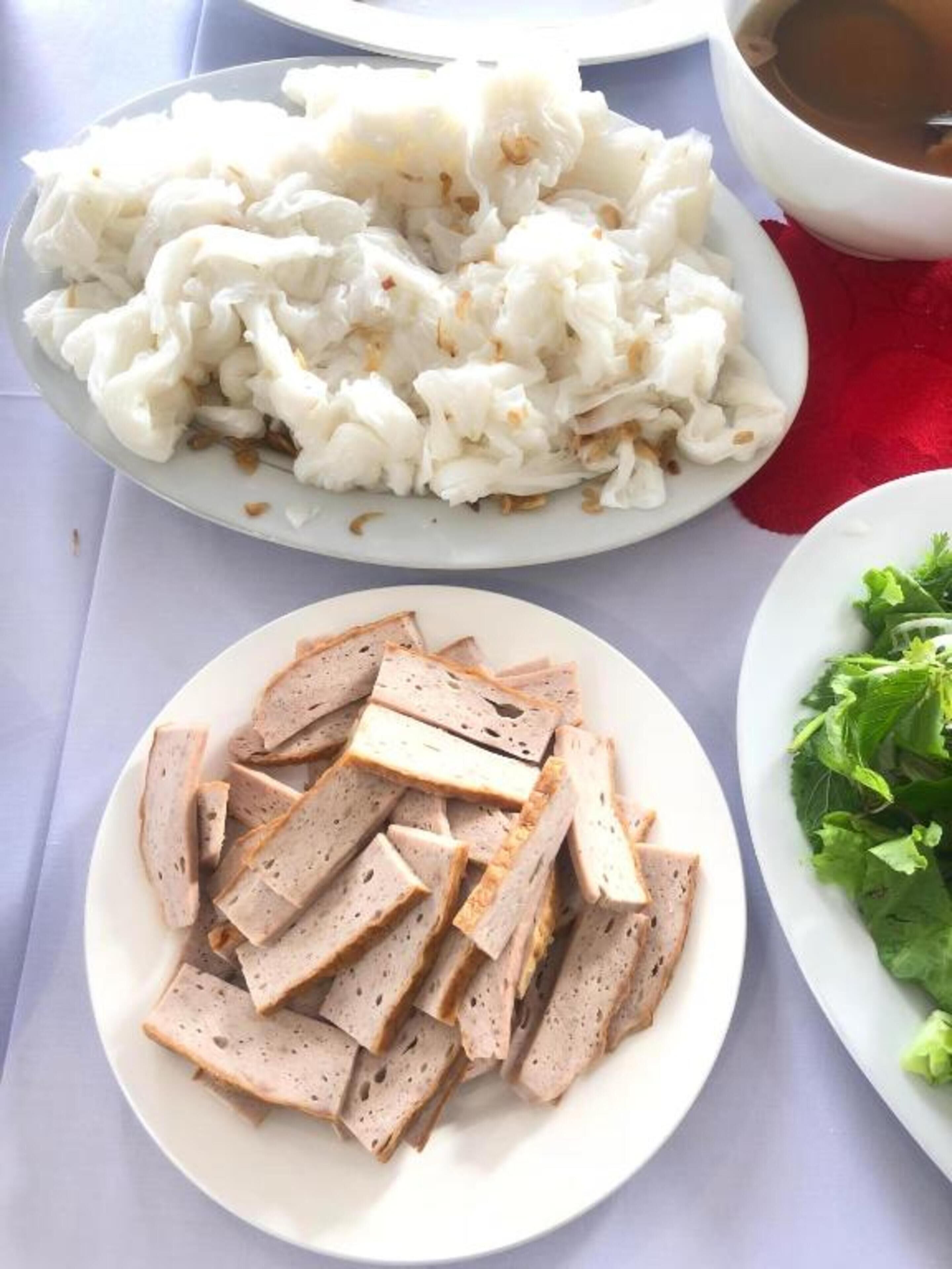 A table with a plate of sliced meat, a plate of white food, and a bowl of soup.