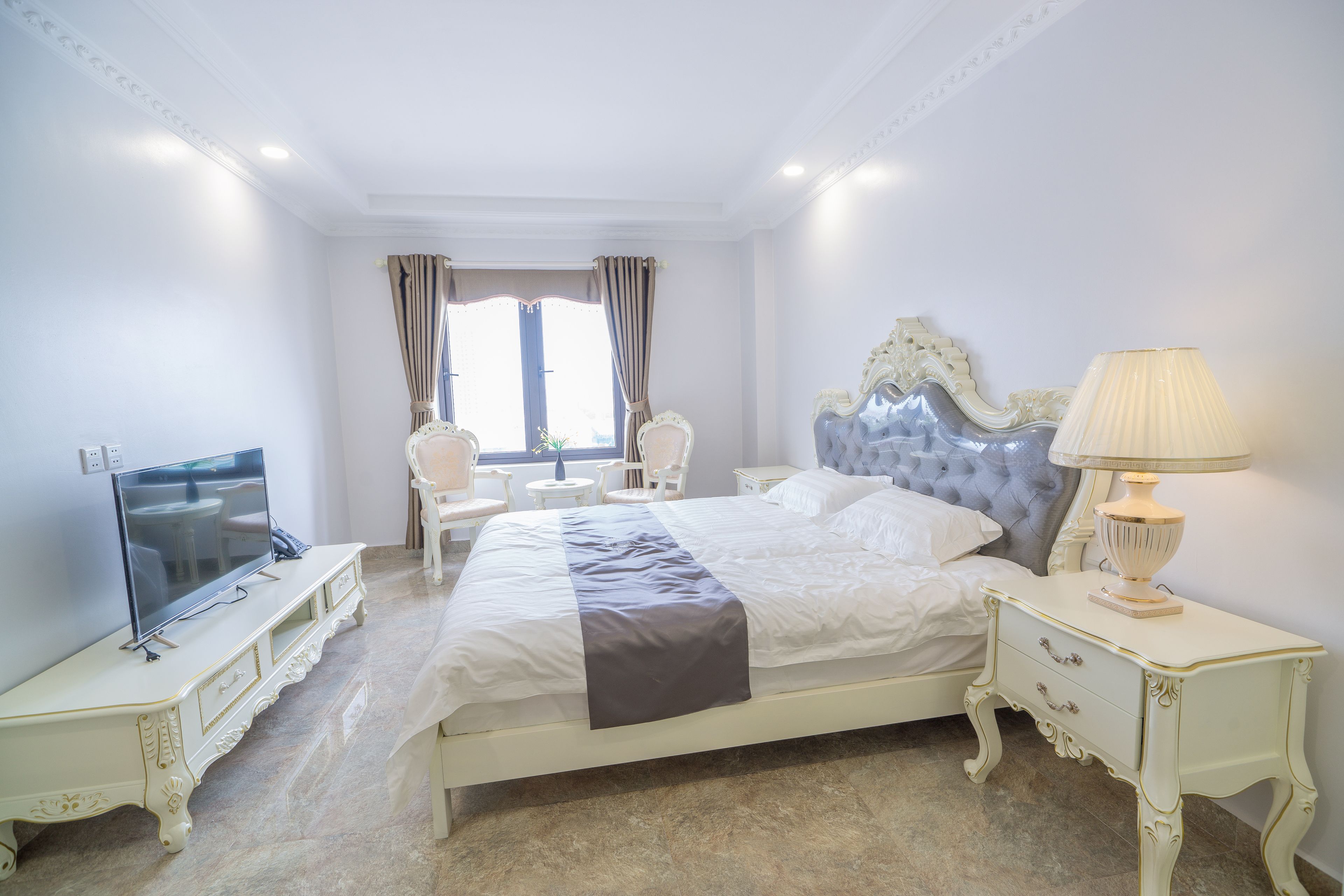 Un dormitorio con una cama grande, un televisor en un mueble, una lámpara y una silla.