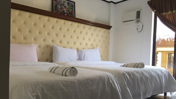 A hotel room with a large bed, a headboard, a wall-mounted air conditioning unit, and a window with curtains. - AV Seven Resort (Boracay Island)