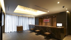 A modern hotel lobby with a marble reception desk, two wooden stools, a wooden cabinet, and a large window with white curtains. - Sotetsu Fresa Inn Tokyo Roppongi (Tokyo)