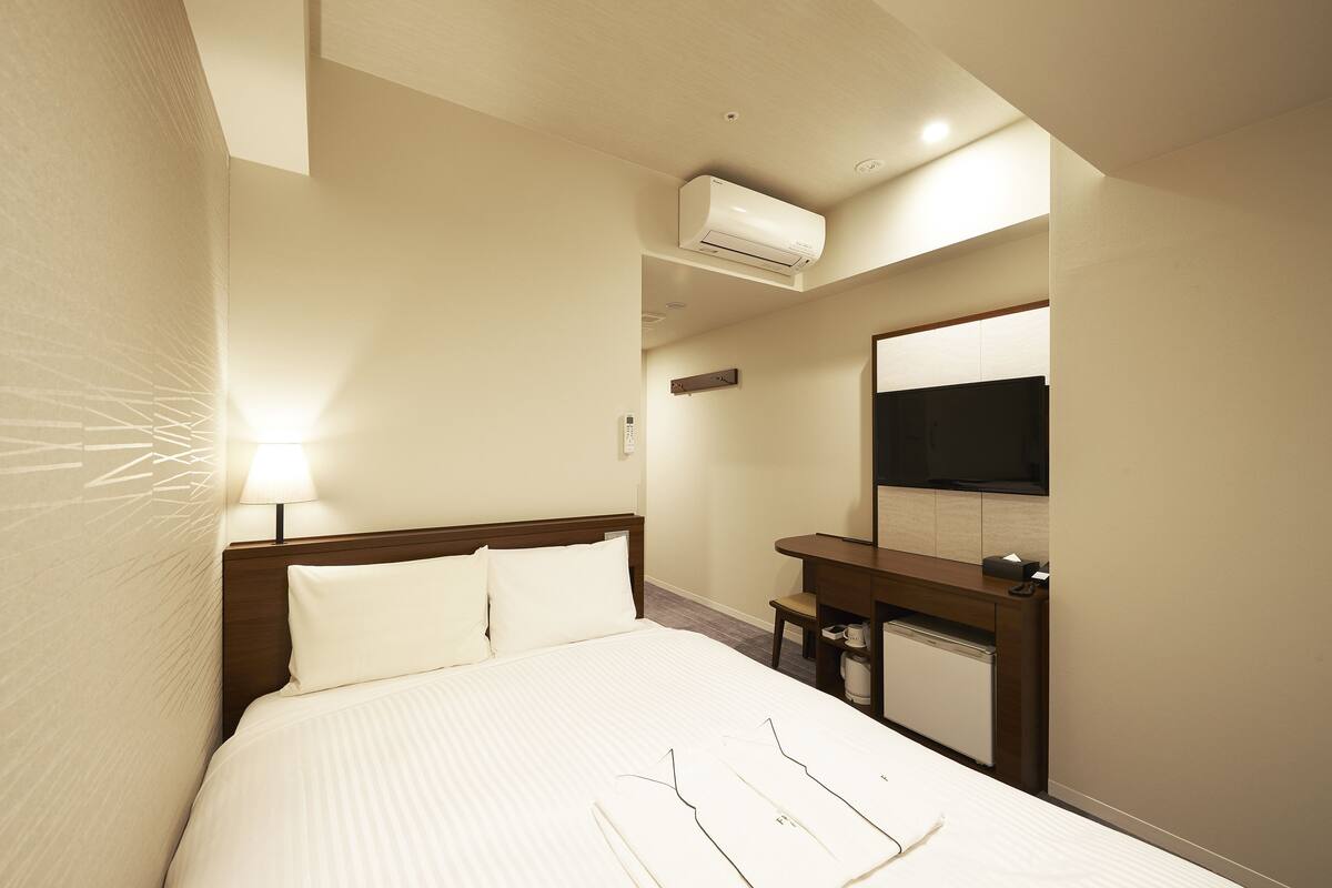 A hotel room with a bed, bedside table, lamp, air conditioning unit, and a mirror.
