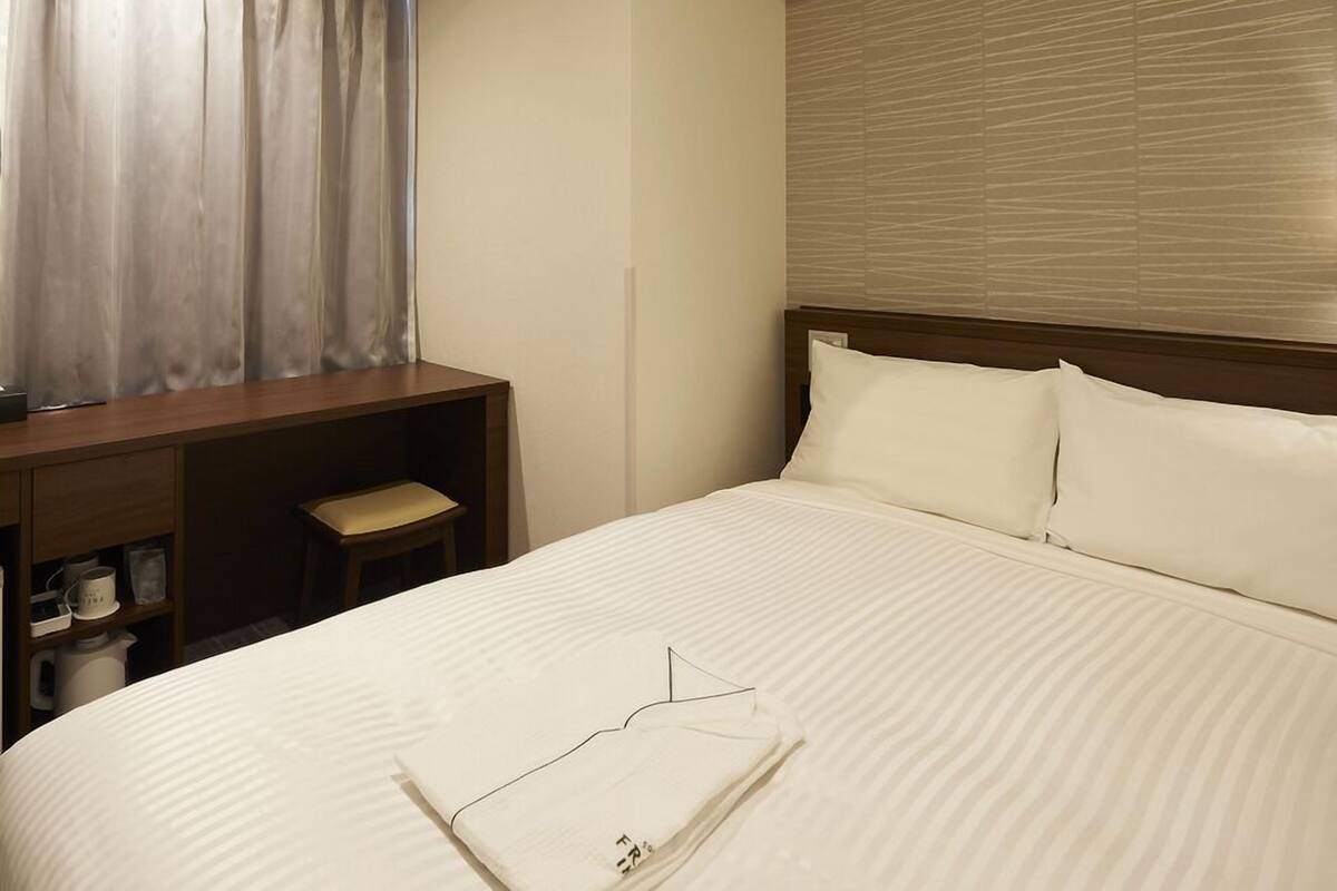 A hotel room with a bed, a desk, a chair, and a window with curtains.