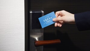 Une main tenant une carte bleue sur laquelle est inscrit le texte « FRESA INN », devant une porte dotée d’une poignée métallique.