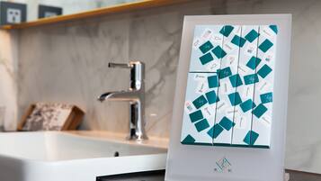 Un baño con lavamanos blanco, grifo moderno y un cartel con formas geométricas y texto.