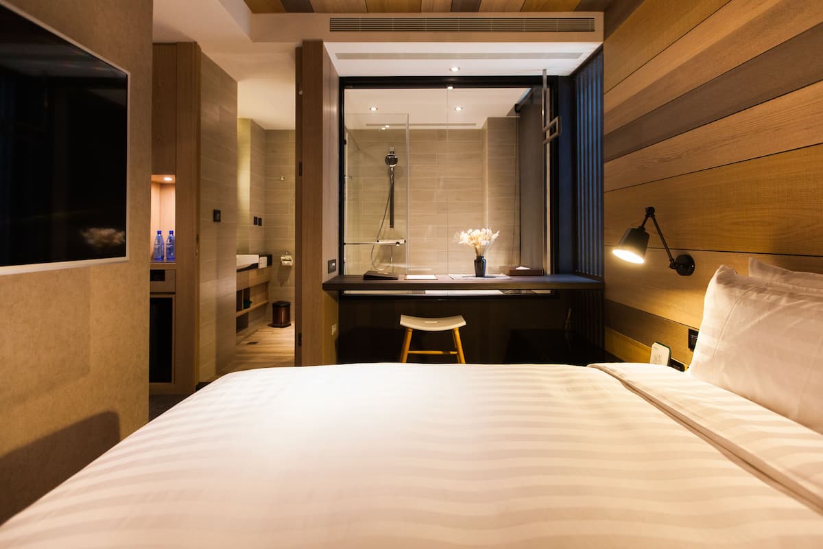 A modern hotel room with a large bed, a desk, and a shower area.