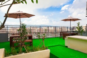A rooftop terrace with two wooden tables, two umbrellas, and a view of the cityscape. - Hotel East Taipei (Taipei)