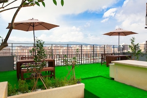 Una terraza en la azotea con dos mesas de madera, dos sombrillas y vistas a la ciudad.