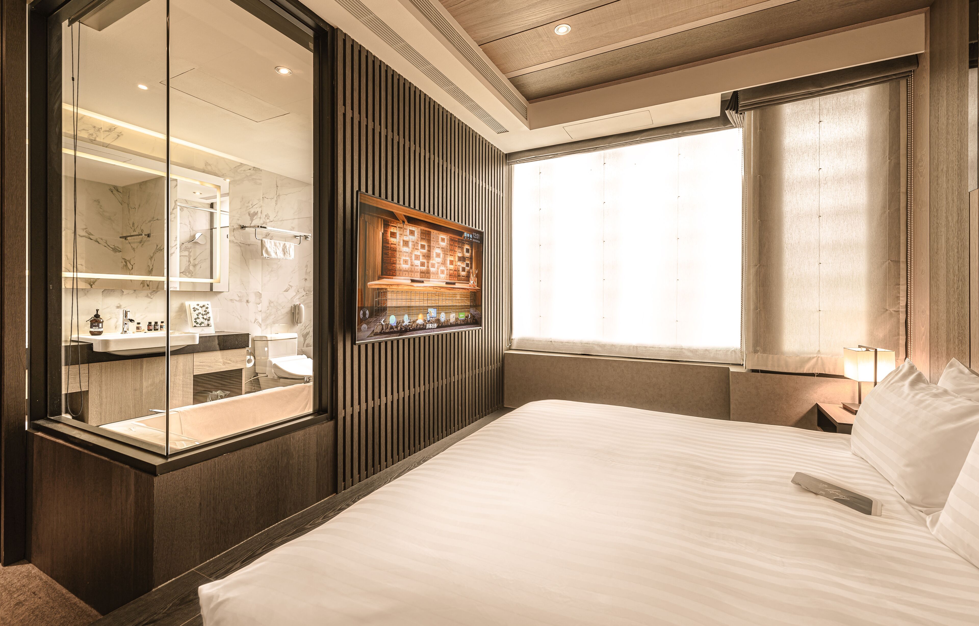 A hotel room with a large bed, a bathroom with a mirror, and a TV mounted on the wall.