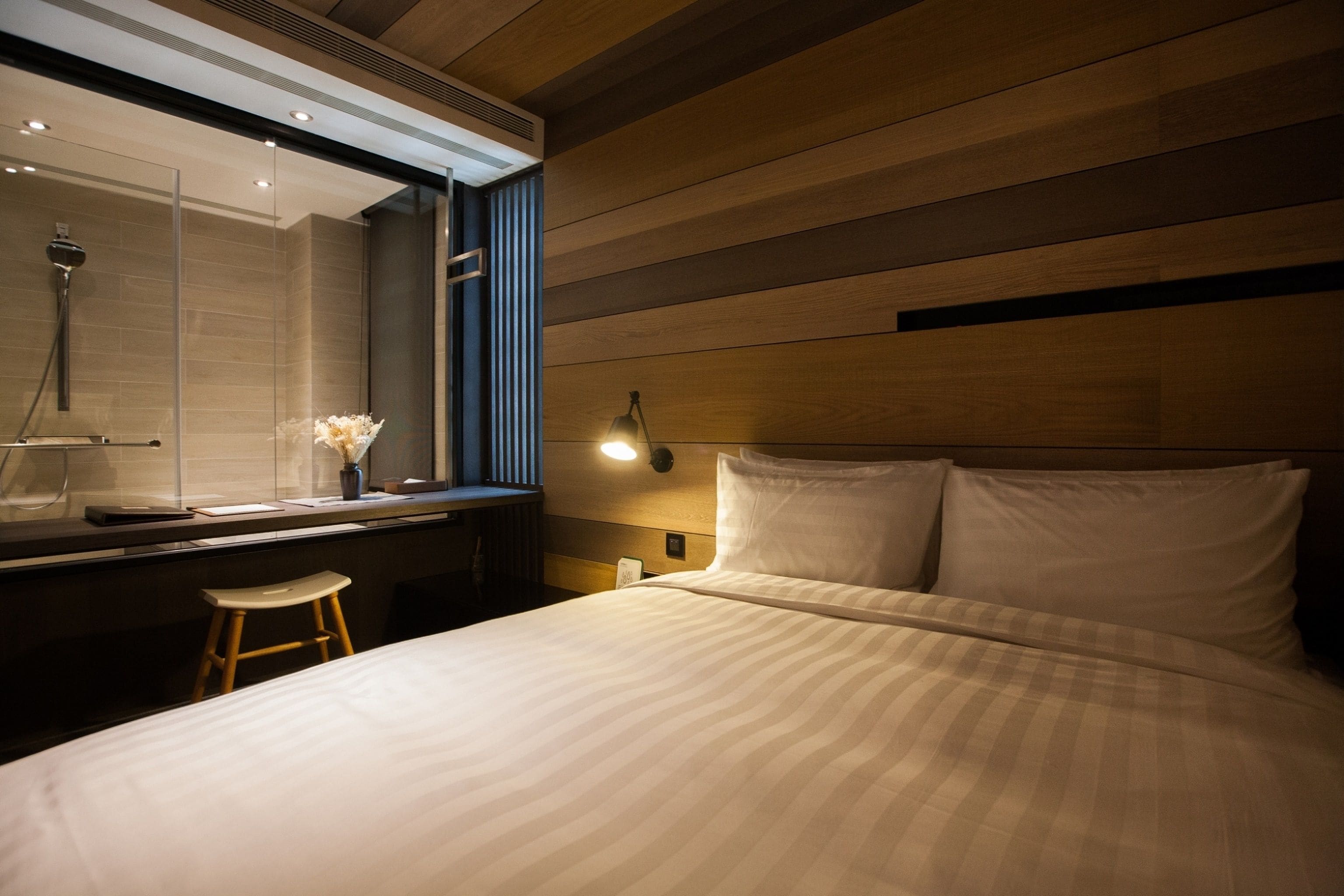 A modern hotel room with a large bed, a wooden headboard, a vanity with a mirror, and a nightstand.