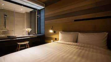 A modern hotel room with a large bed, a wooden headboard, a vanity with a mirror, and a nightstand.