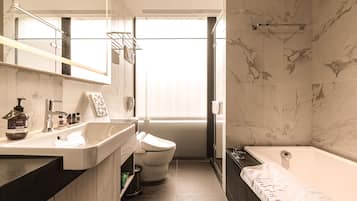 Une salle de bain moderne avec un mur en marbre, une baignoire, des toilettes et un lavabo équipé de produits de toilette.