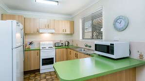 A compact kitchen with wooden cabinets, a white refrigerator, a stove, a microwave, and a green countertop.