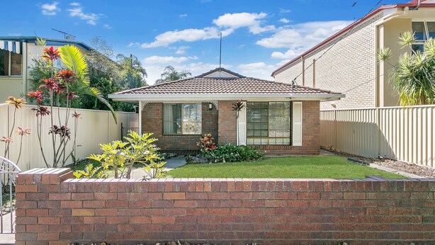 A residential house with a tiled roof, brick exterior, and a well-maintained front yard with various plants.