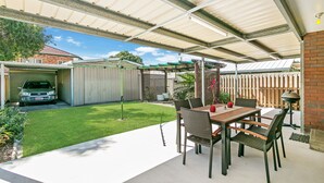 A covered patio with a table and chairs, a car in the background, and a fenced yard.