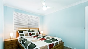A bedroom with a wooden bed, a nightstand with a lamp, and a ceiling fan.