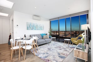 A modern living room with a dining area, large windows, and a city view. - StayCentral - Northcote Hill Penthouse (Northcote)