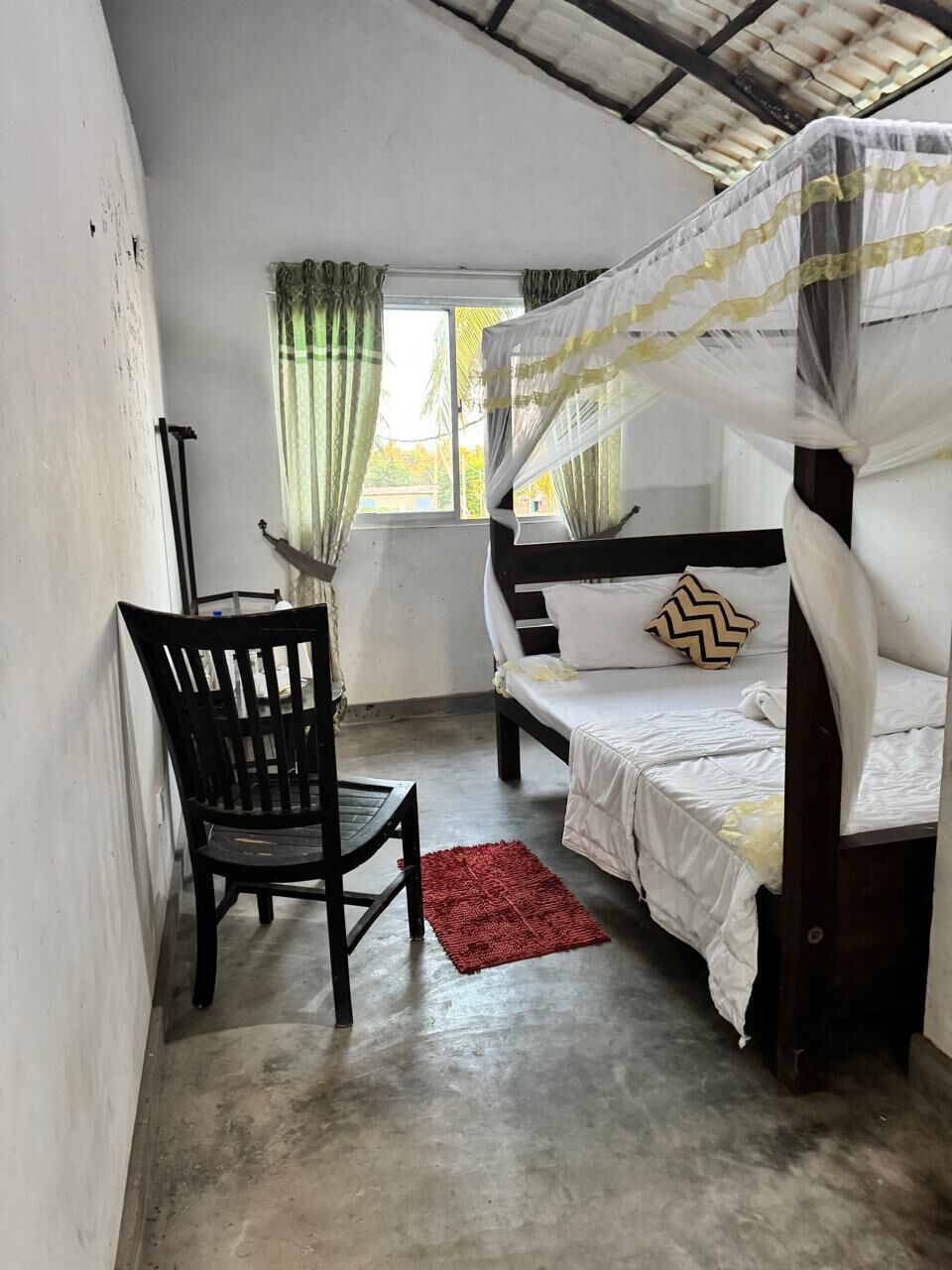 A room with a bed, a chair, a window with curtains, and a red rug.