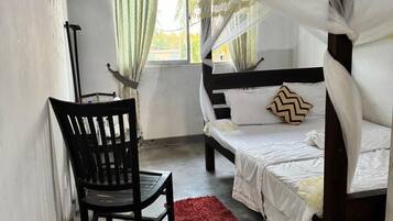 A room with a bed, a chair, a window with curtains, and a red rug.