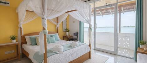 A four-poster bed with a canopy, a bedside table with a plant, and a view of the sea through a sliding glass door.