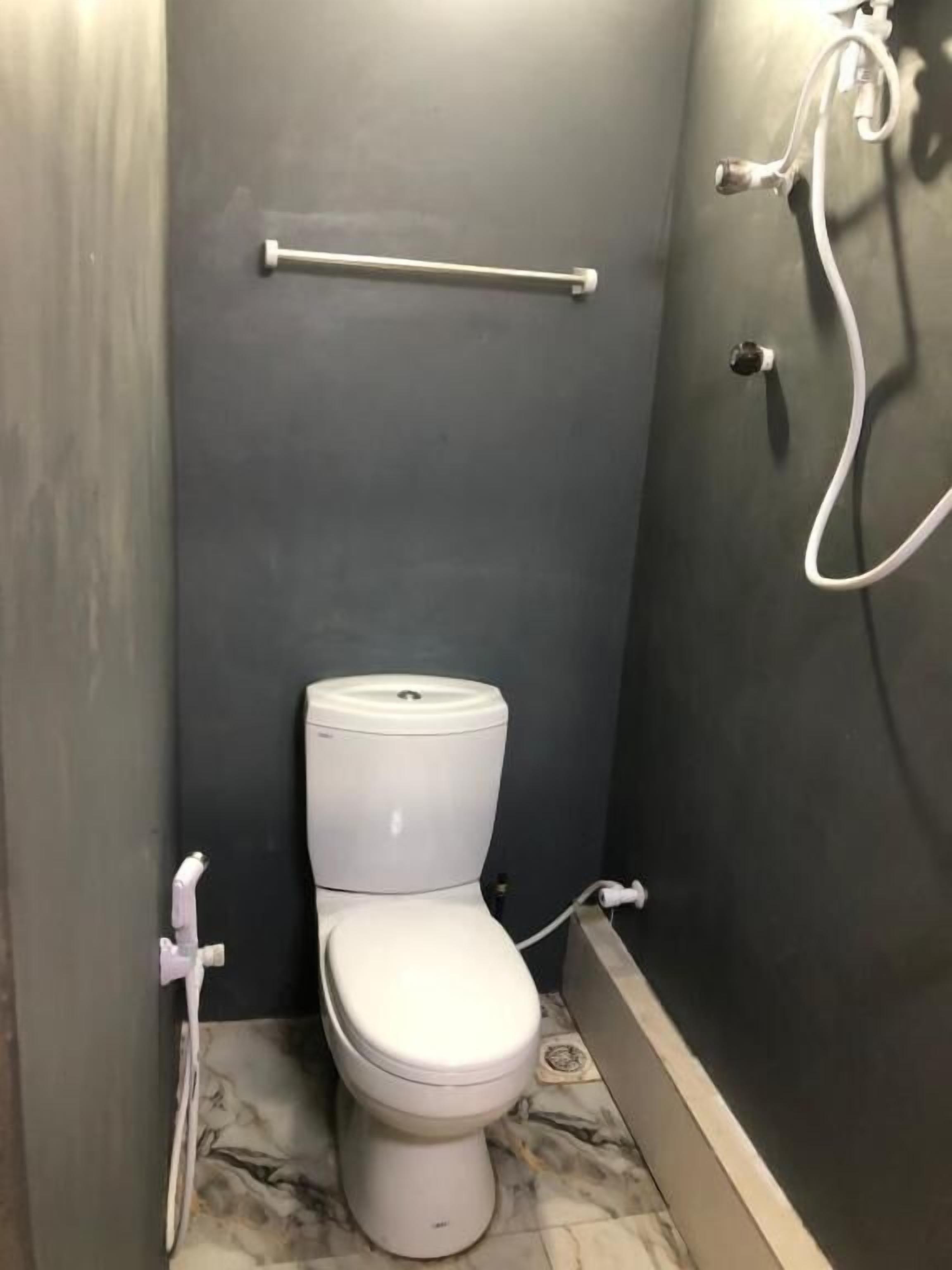 Un baño pequeño y moderno con inodoro, secamanos y manguera de ducha.
