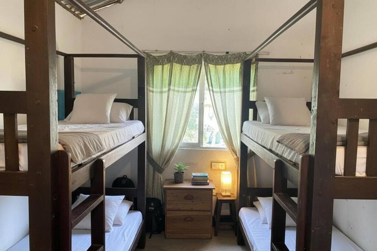 Habitación con literas de madera, una mesita de noche con lámpara y una ventana con cortinas.