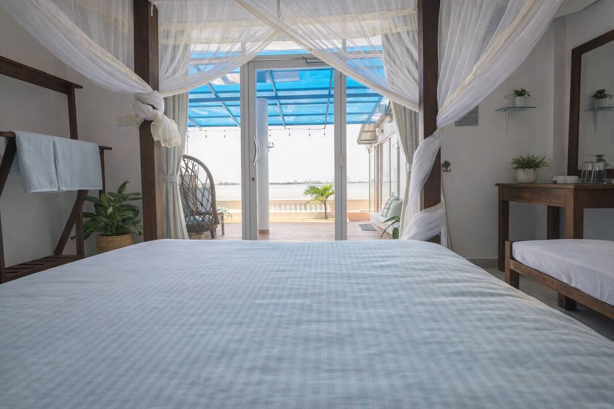 Un dormitorio con una cama grande, una silla, una mesita y vistas al mar a través de un ventanal.