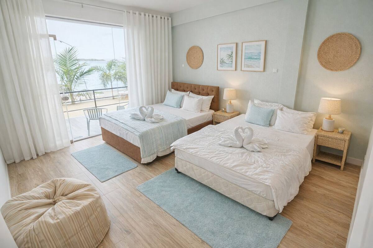 Habitación de hotel con dos camas, un balcón con vista al mar y una pequeña zona de estar.