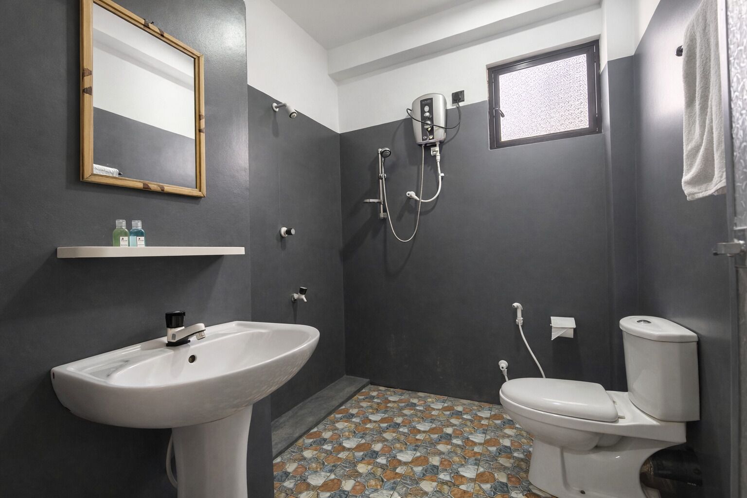 A bathroom with a white sink, a toilet, and a shower. There is a mirror on the wall and a shelf with toiletries.