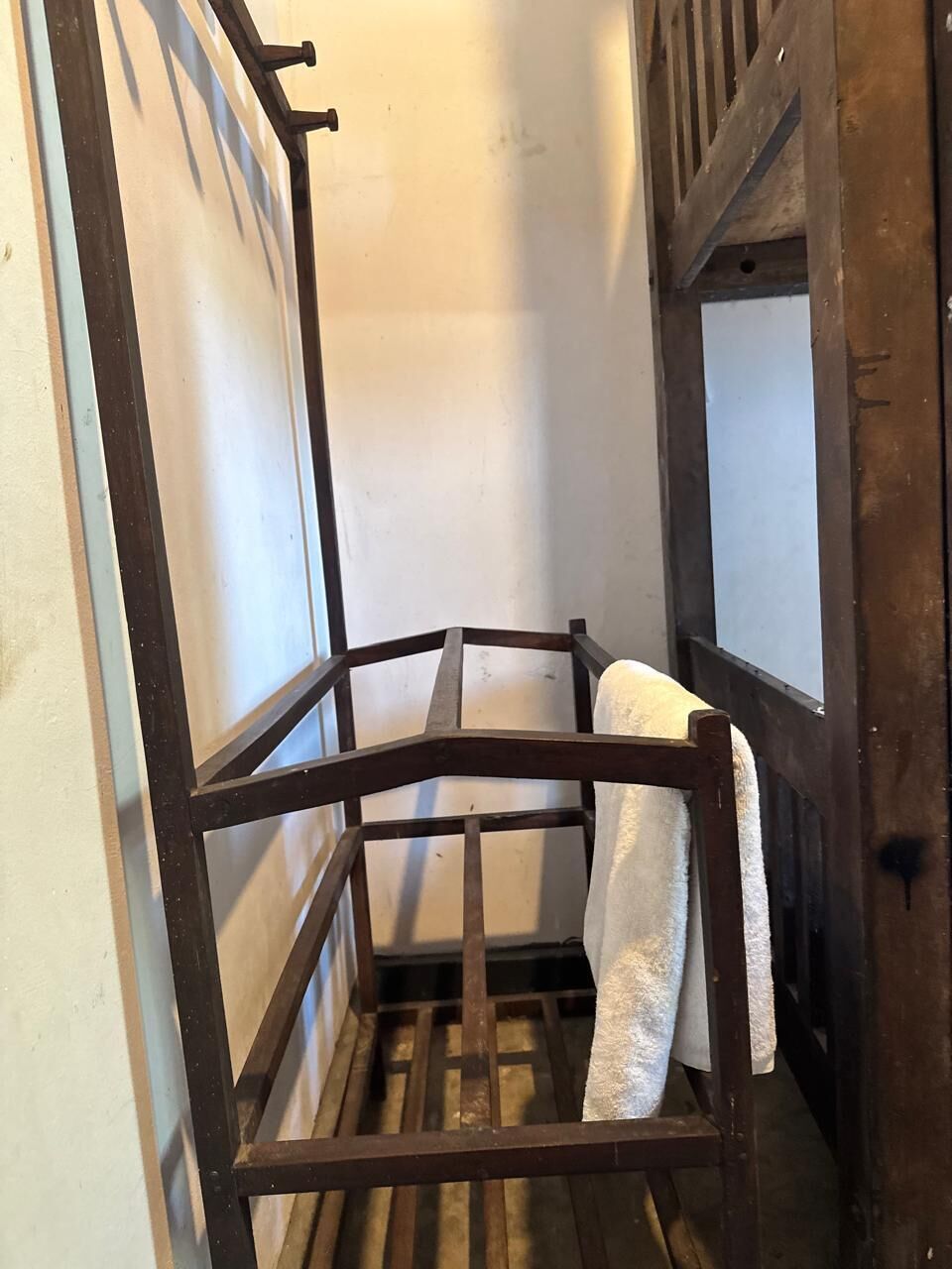 A corner of a room with a wooden bench and a towel hanging on the wall.