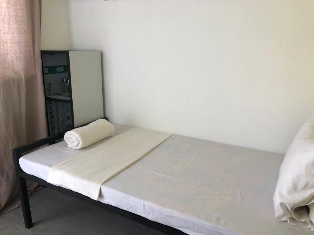 A single bed with a white mattress and a rolled white towel, a white pillow, and a white blanket.