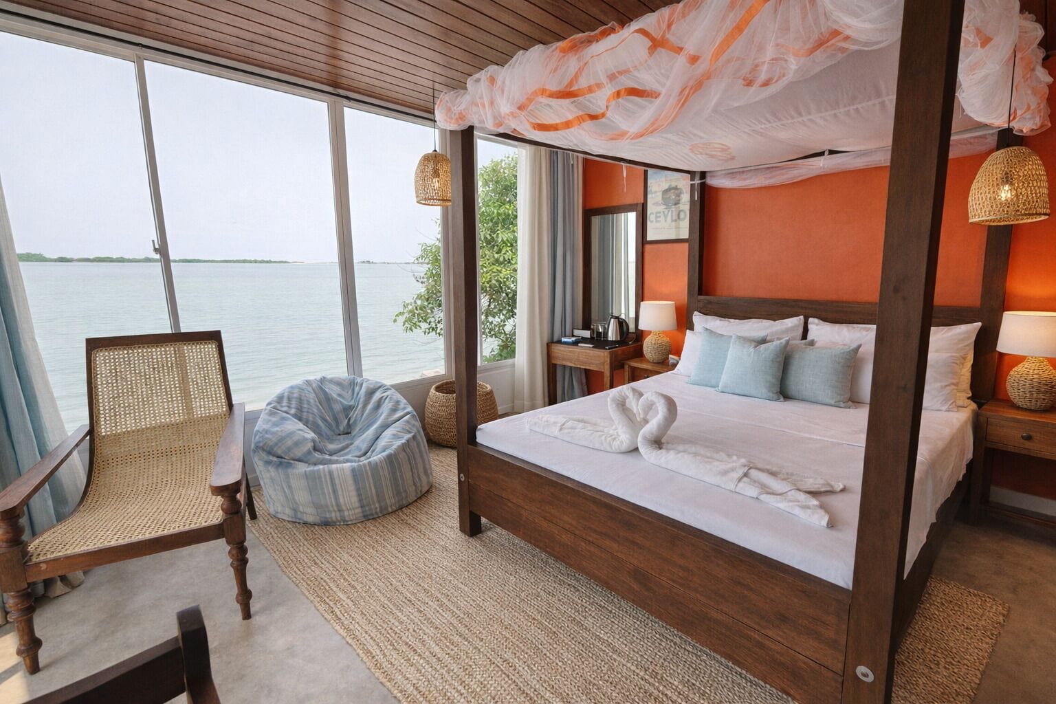 A four-poster bed with a canopy, a wicker chair, and a view of the sea.