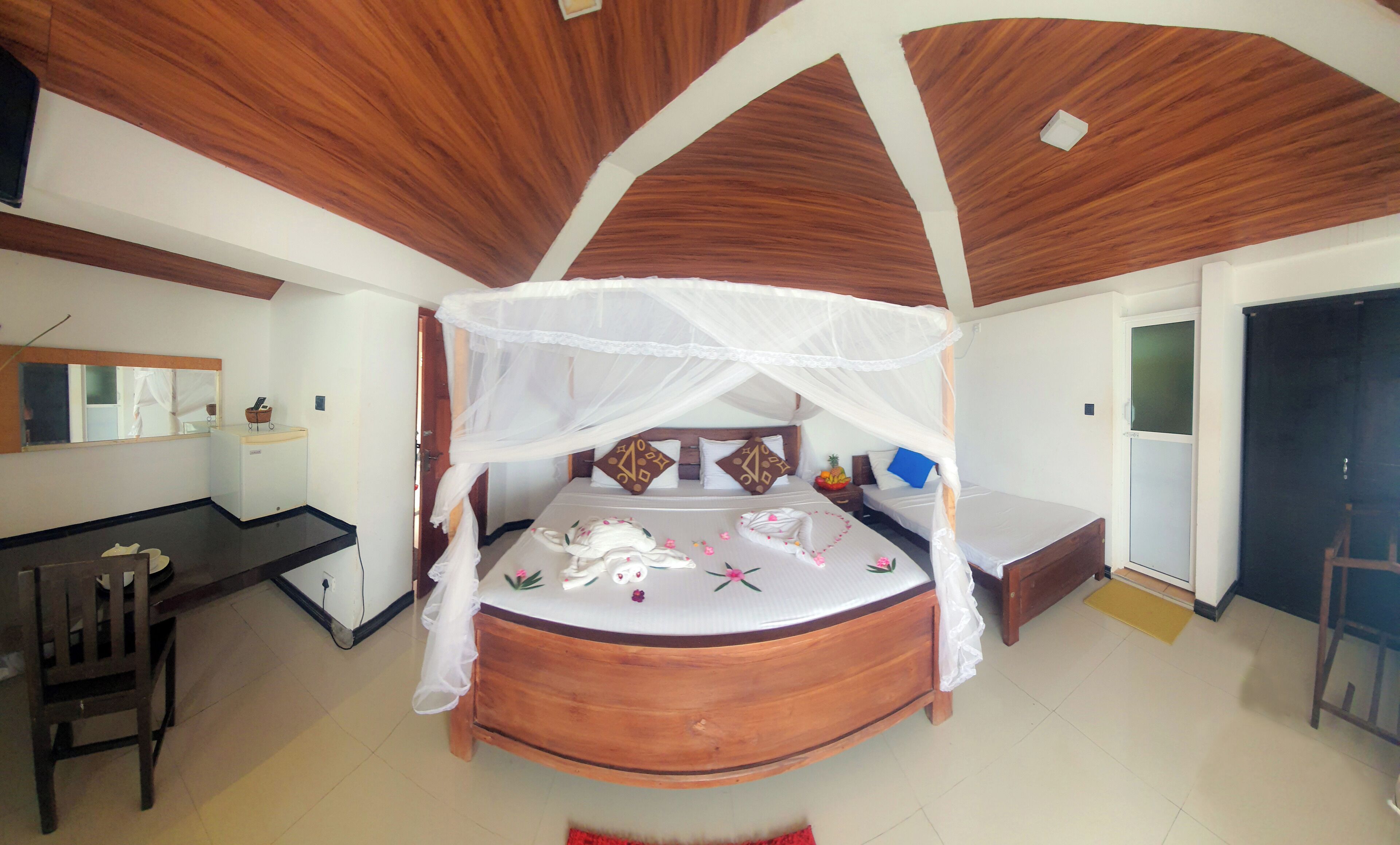A bedroom with a wooden ceiling, a bed with a canopy, a desk, and a chair.